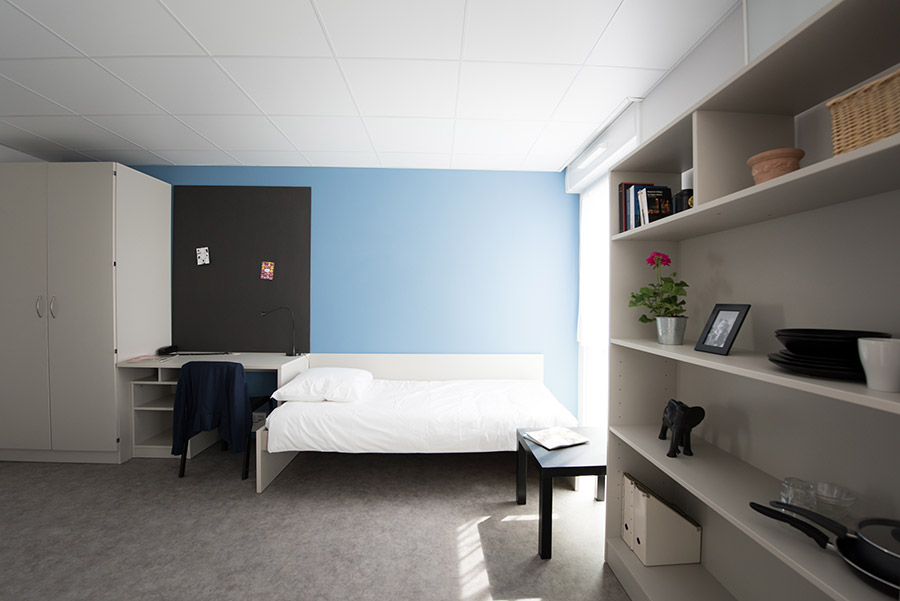 Chambre étudiante avec un lit, un bureau, une armoire et une étagère